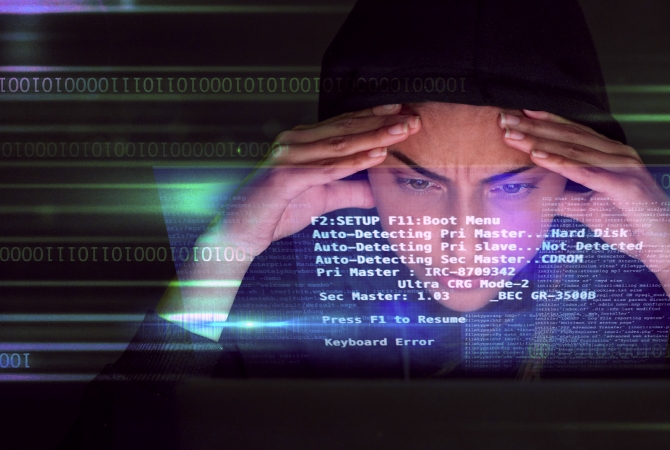 Overview: A person in a hoodie looks at a screen filled with computer code and error messages, offering an overview of hacking or cybersecurity activity.